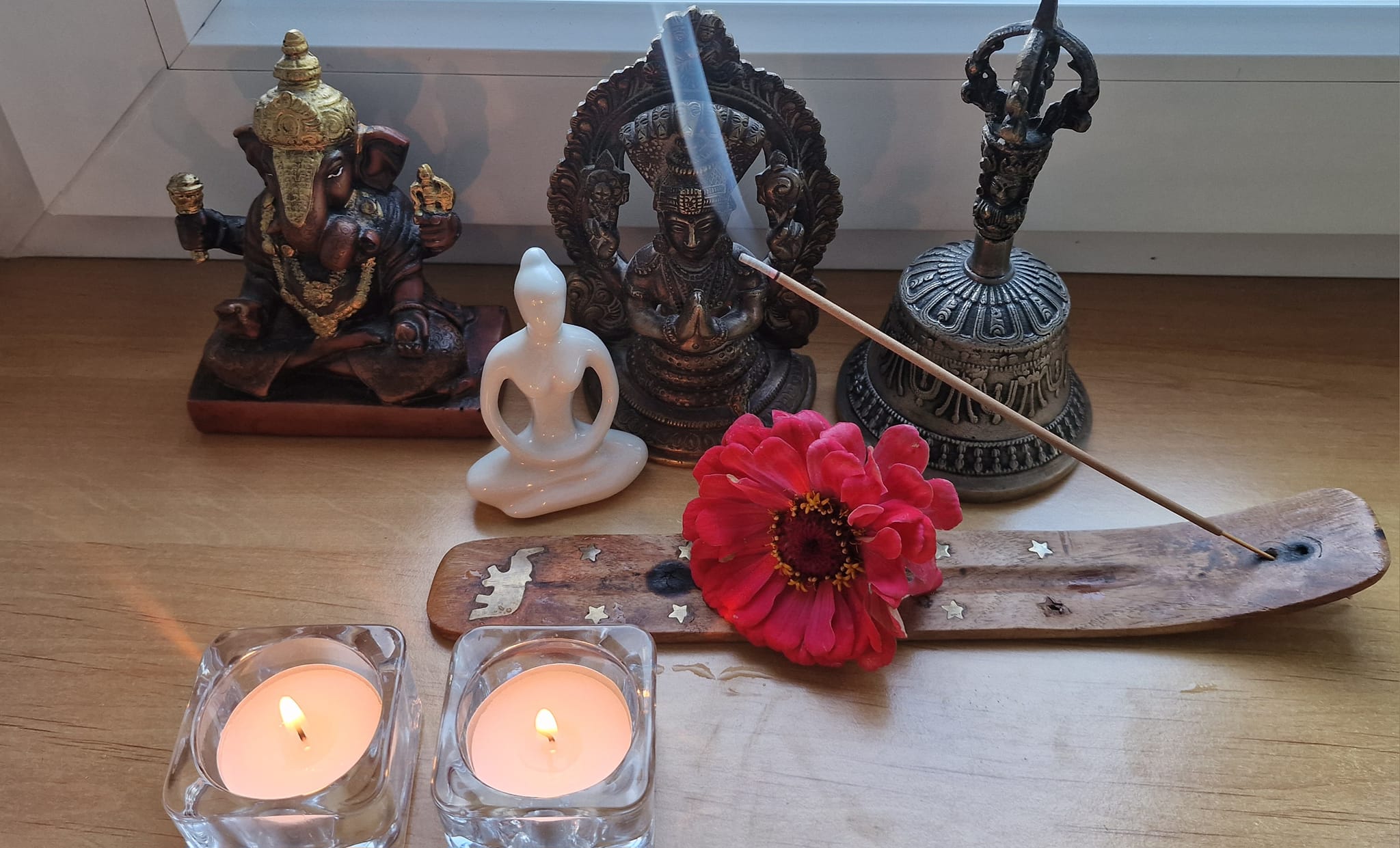 figurki i dzwonek na parapecie, świeczki, palące się kadzidełko z kwiatkiem