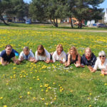 kobiety leżące na trawie pełnej kwiatów, uśmiechające się.